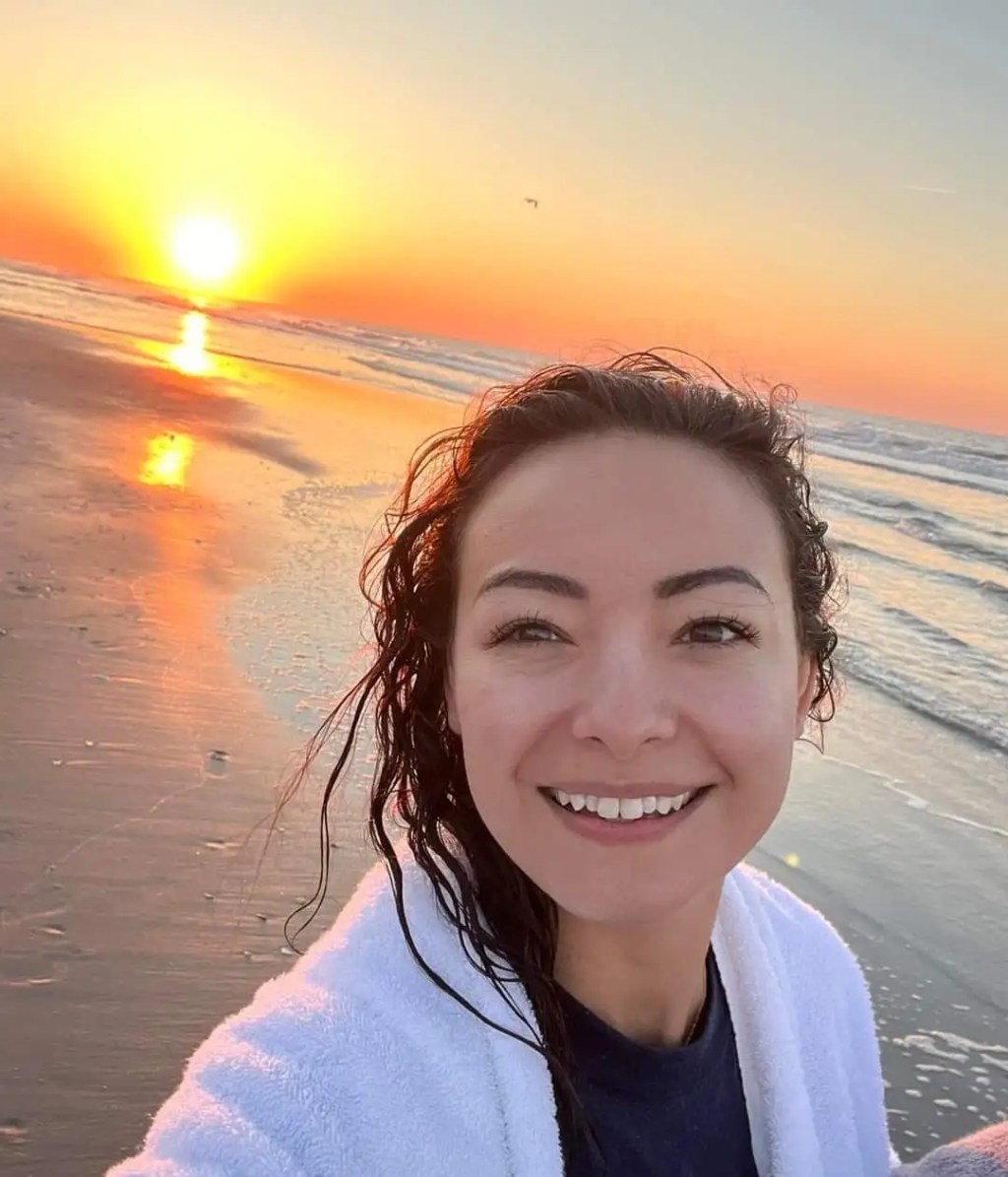 Mica Miller smiling on a beach at sunset.